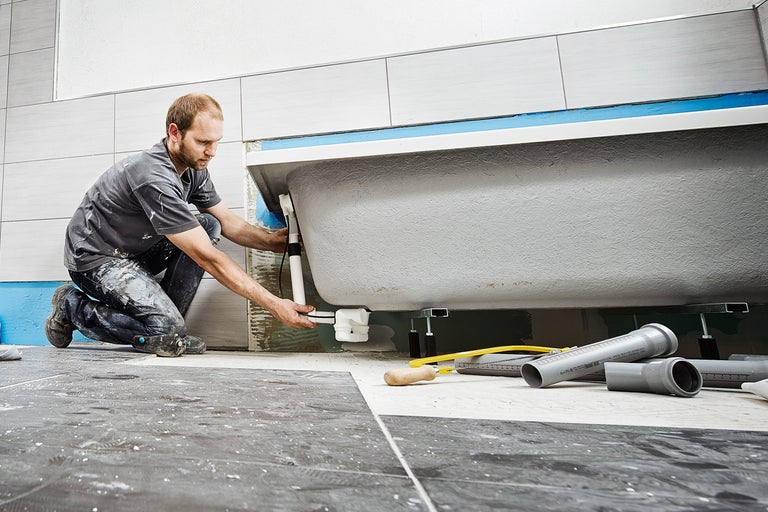 Installatör ansluter avloppsrör till ett badkar i ett badrum