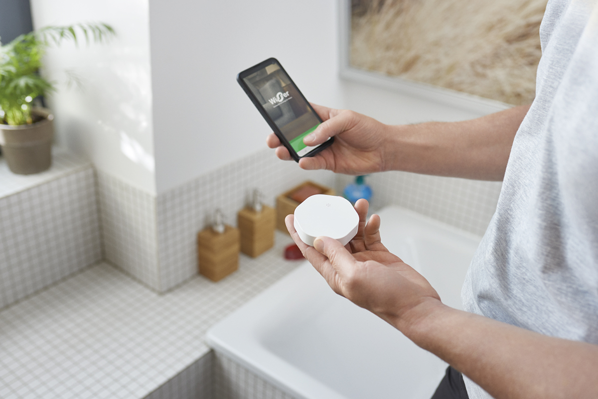 Person som håller en smart hem-enhet och en smartphone i ett badrum.