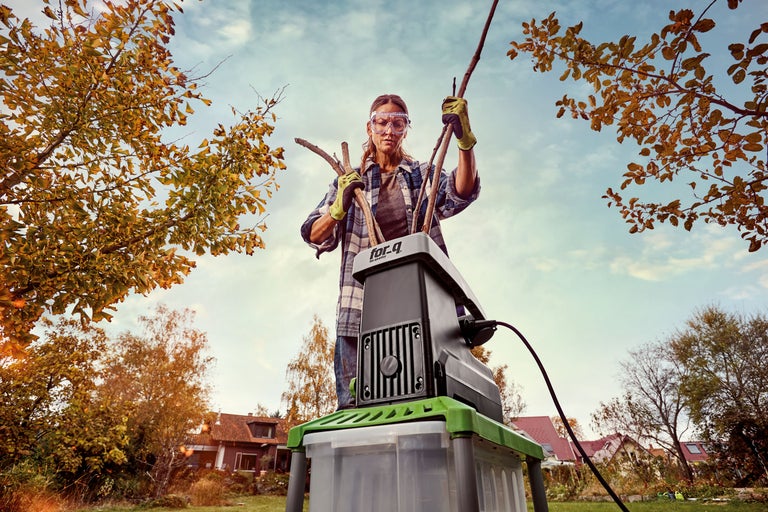 En kvinna använder en trädgårdshackare för att hacka grenar.