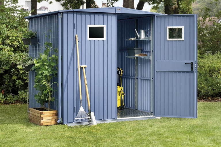 Trädgårdsskjul med öppen dörr, fönster och hyllor, omgiven av växter och trädgårdsredskap