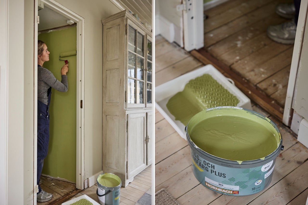 En kvinna målar en vägg grön med en roller. I förgrunden står en hink Hornbach Väggfärg och takfärg på ett trägolv.