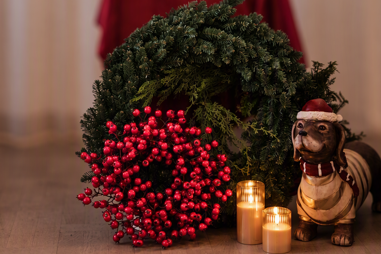 Juldekoration med adventskrans av grankvistar, röda bär, två ljus och en taxfigur med julmössa.