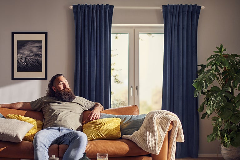 Vardagsrum med brun lädersoffa, blå gardiner och en krukväxt