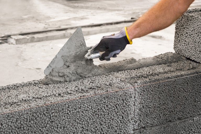 En murare applicerar murbruk på lättbetongblock med en murslev