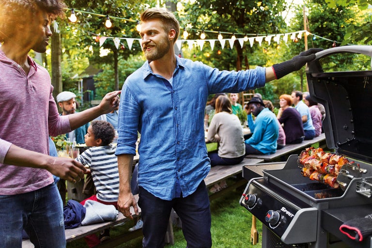 Grillscen utomhus med män, kvinnor och barn runt en grillplats med Weber Spirit gasolgrill.