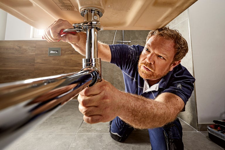 En man reparerar en vattenlås under ett handfat med en skiftnyckel i badrummet.