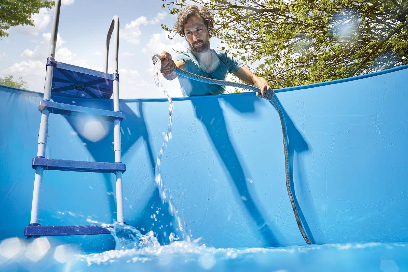 Man fyller pool med vattenslang och stege