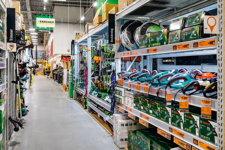 Gångvy i en Hornbach-butik med hyllor fulla av trädgårdsredskap som trimmare, häcksaxar och sekatörer från varumärkena Kärcher, Bosch och Gardena.