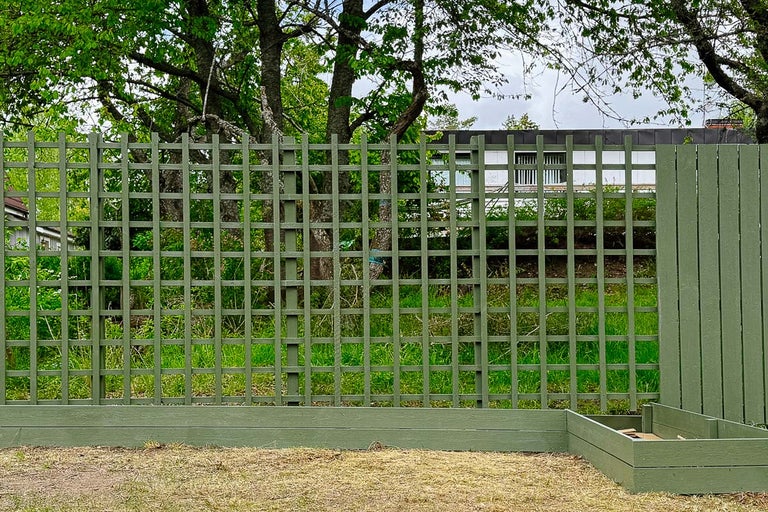 Trästaket med gallerstruktur och upphöjd rabatt i trädgården
