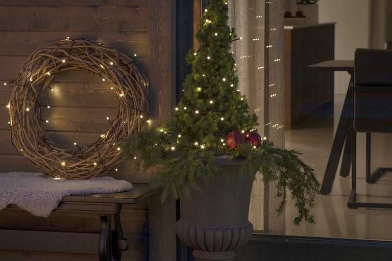 Dekorativ scen med upplyst krans, liten julgran i kruka och ljusslinga
