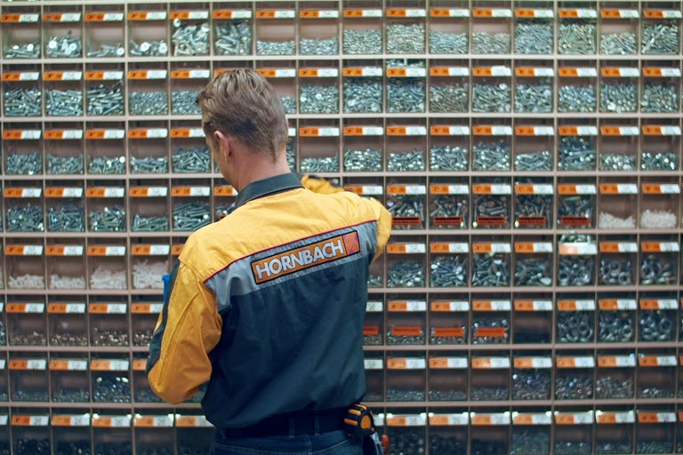 En Hornbach-anställd står framför en hylla med skruvar och annat fästmaterial.