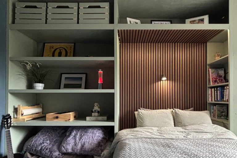 Sovrumsinredning med integrerad vägghylla, ribbvägg i trä som sänggavel och indirekt belysning i modern bostadsatmosfär.