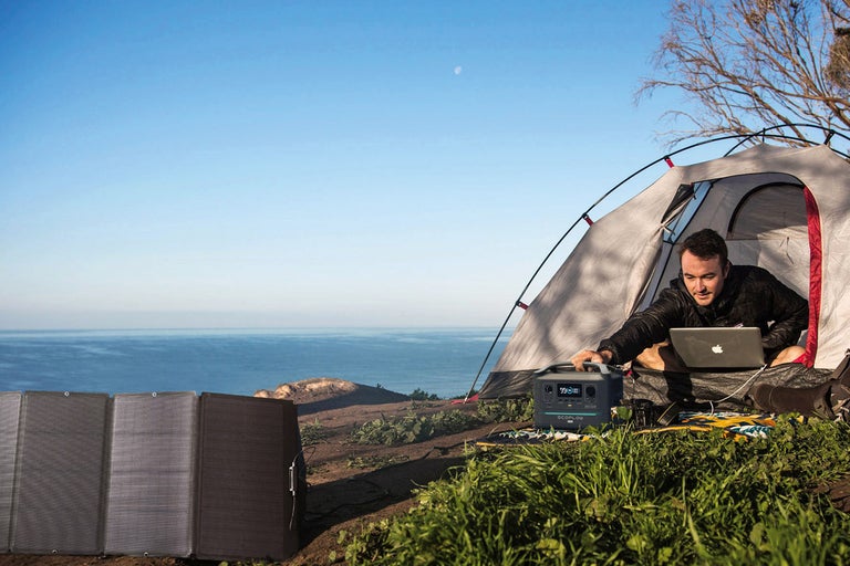 Campingscen med tält, person med bärbar dator, solpanel och kraftstation för nätansluten elförsörjning