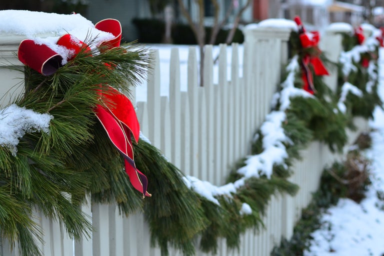 Juldekoration med grangirlang och band på ett trädgårdsstaket