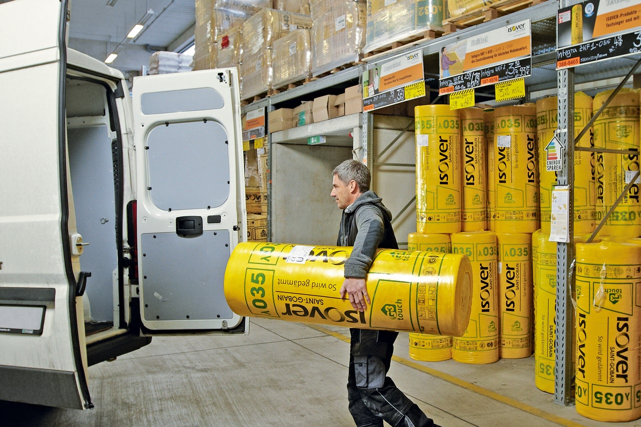 Man bär en rulle Isover isoleringsull till en skåpbil i ett lager