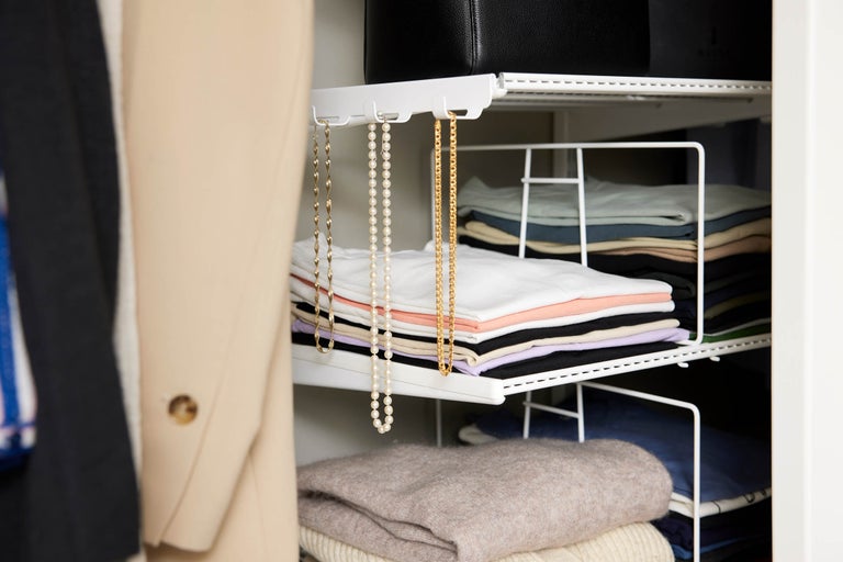 Interiör av en garderob med kläder och smycken på en vit stång