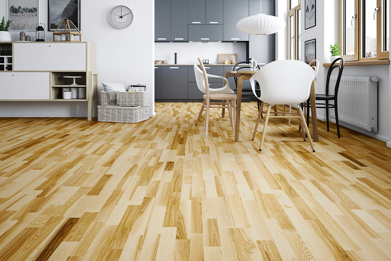 Träparkett i skeppsgolvsdesign i en ljus, modern matplats med intilliggande kök.
