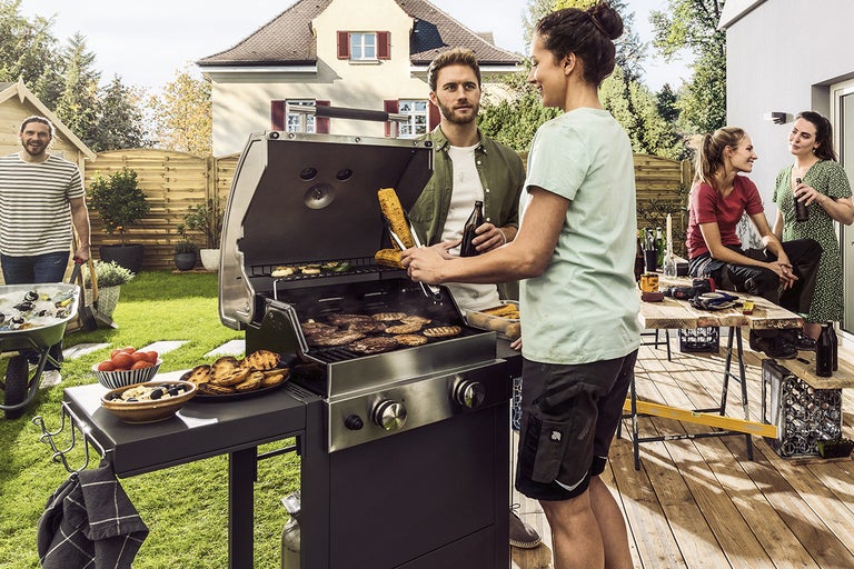 Scen med en gasolgrill i trädgården med flera personer som grillar