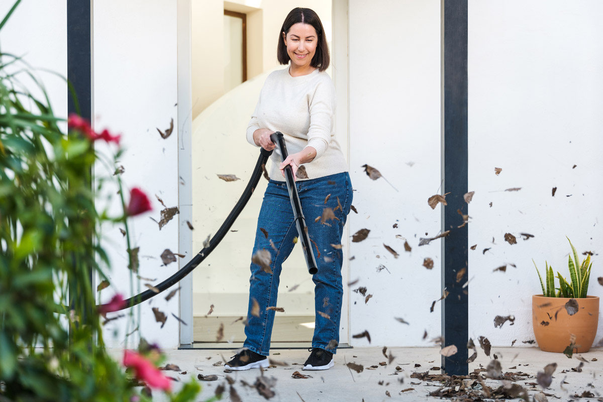 Kvinna använder en lövsug för att rengöra en terrass.