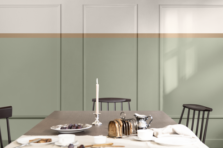Matsal med väggpaneler i ljusgrönt och beige, accentuerat av en horisontell rand, med ett dukat matbord och trästolar.