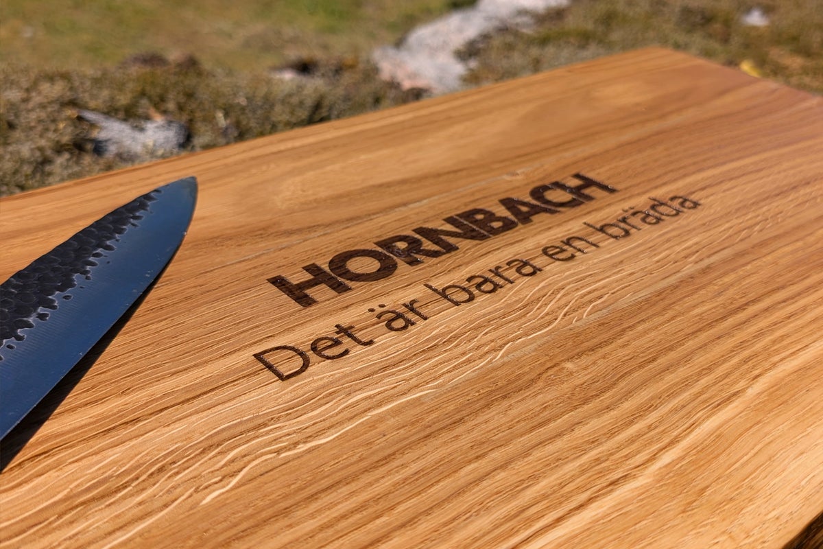 Träbräda med Hornbach Logo och ingraverad text Det är bara en bräda bredvid en kniv.