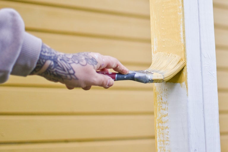 En person målar en trästruktur med en pensel och färg.