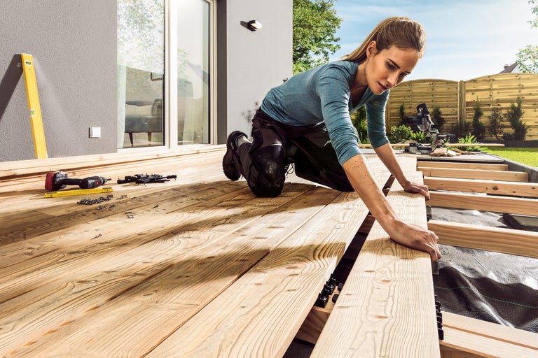 Kvinna lägger träterrass i trädgården med verktyg och skruvar