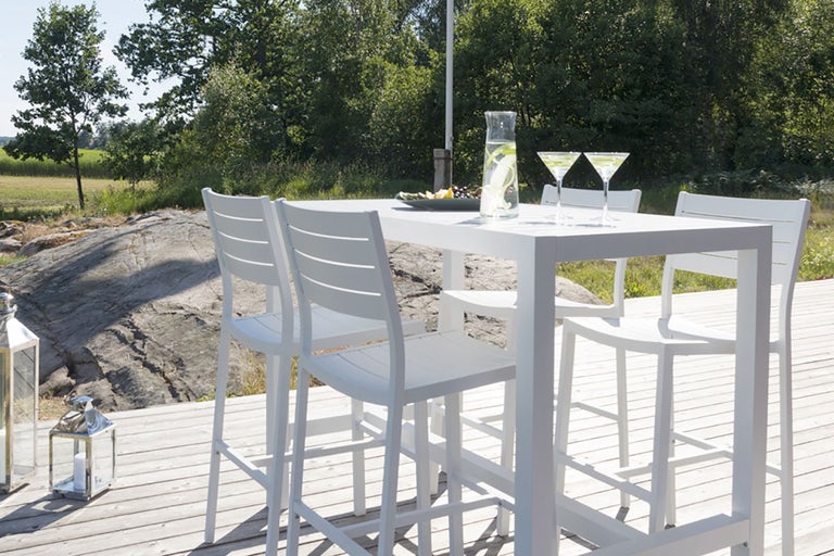 Vit trädgårdsmöbelset med bord, barstolar, glas och dekoration utomhus