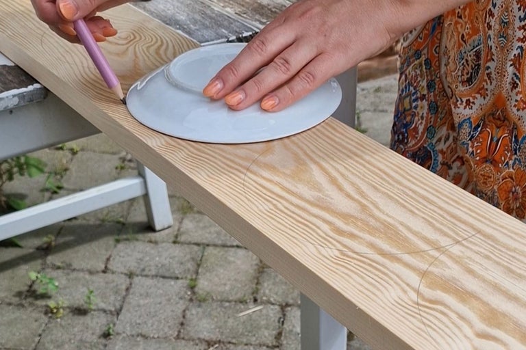 En person ritar en cirkel runt en tallrik på en träbräda med en penna.