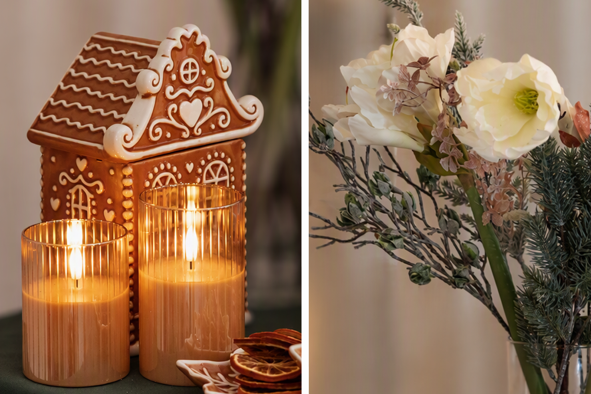 Julbordsdekoration med pepparkakshus i keramik, räfflade lyktor med ljus och en bukett med konstgjorda blommor.