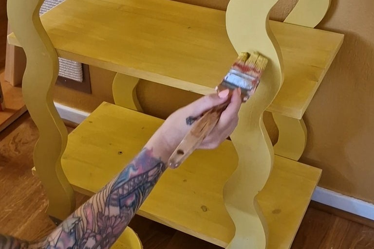 En person målar en trahylla med en pensel.