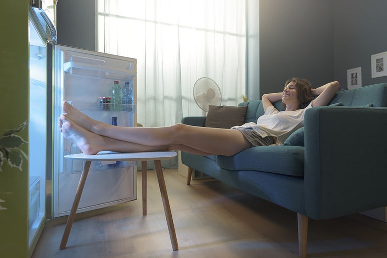 Kvinna kopplar av i en soffa med fötterna på ett bord framför ett öppet kylskåp