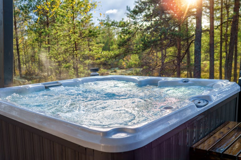 Bubblig, fyllt badtunna med trätrappor utomhus framför träd