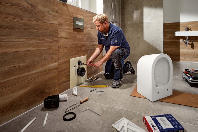 En hantverkare installerar en toalett i ett badrum med träpaneler