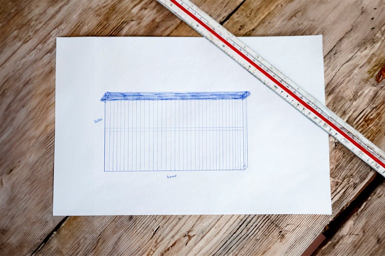 Handritad skiss av en byggnadsplan med mått på papper och en linjal.