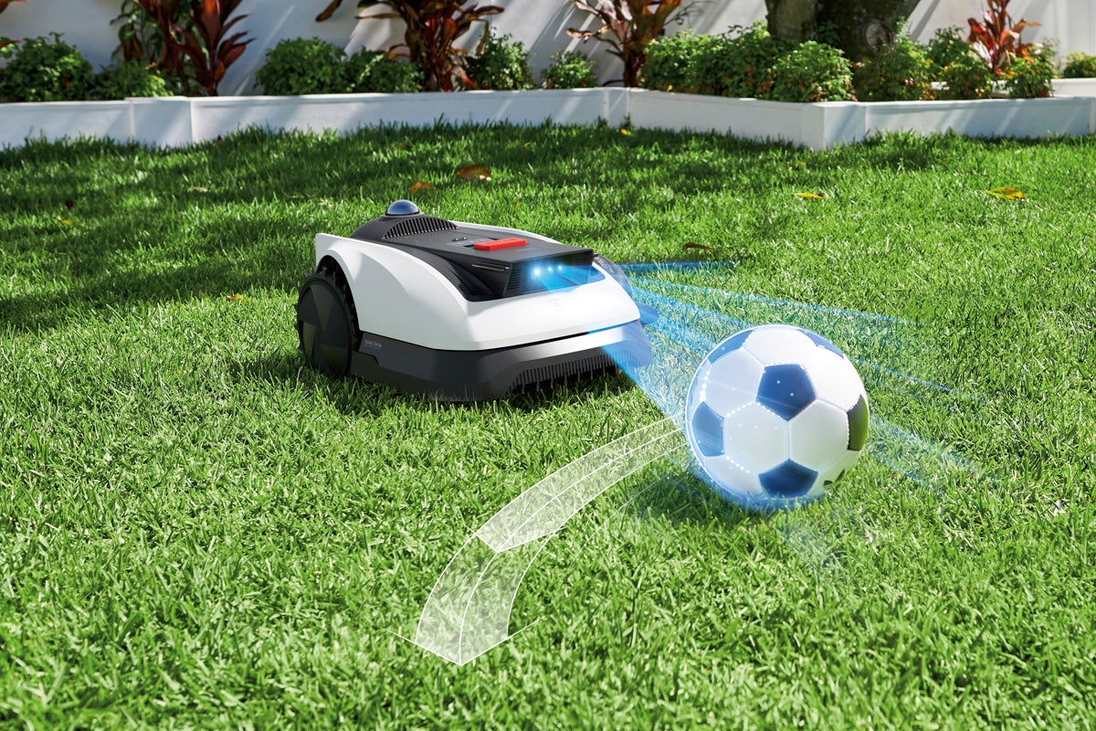Robotgräsklippare med hinderdetektering som undviker en fotboll på gräsmattan.