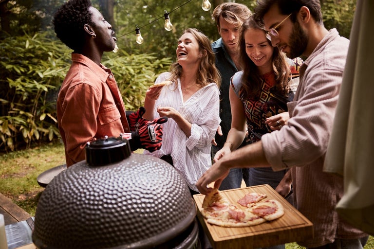 En grupp vänner grillar pizza utomhus med en keramisk grill.