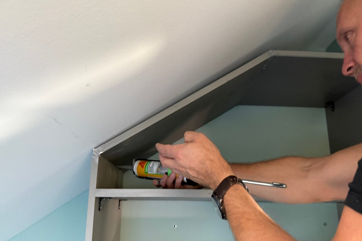 Hantverkare förseglar en fog mellan skåp och tak med tätningsmedel