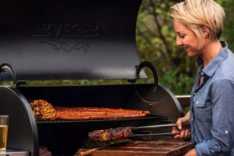 Kvinna grillar kött och grönsaker på en utomhusgrill.