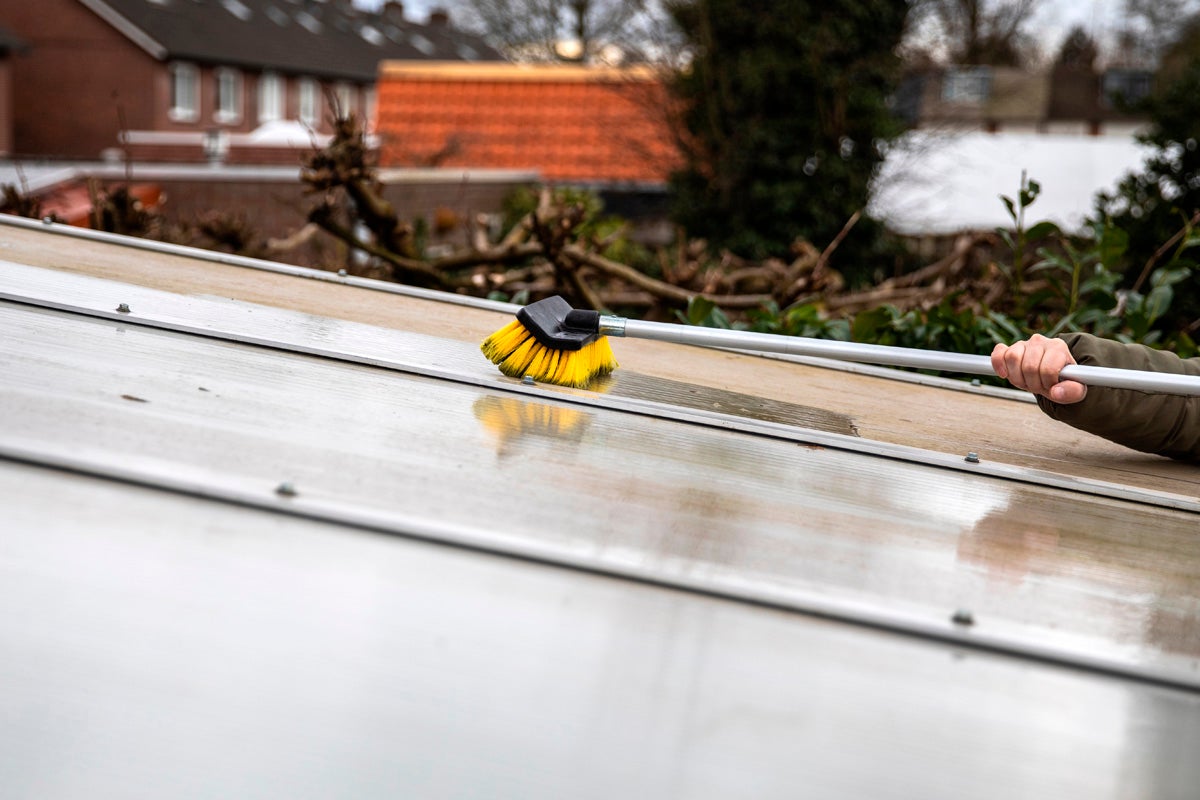 Rengöring av ett transparent terrasstak med en teleskopborste