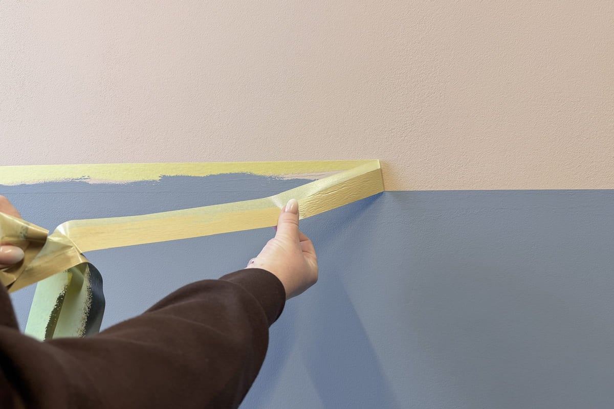 En person fäster maskeringstejp på en vägg målad i två färger