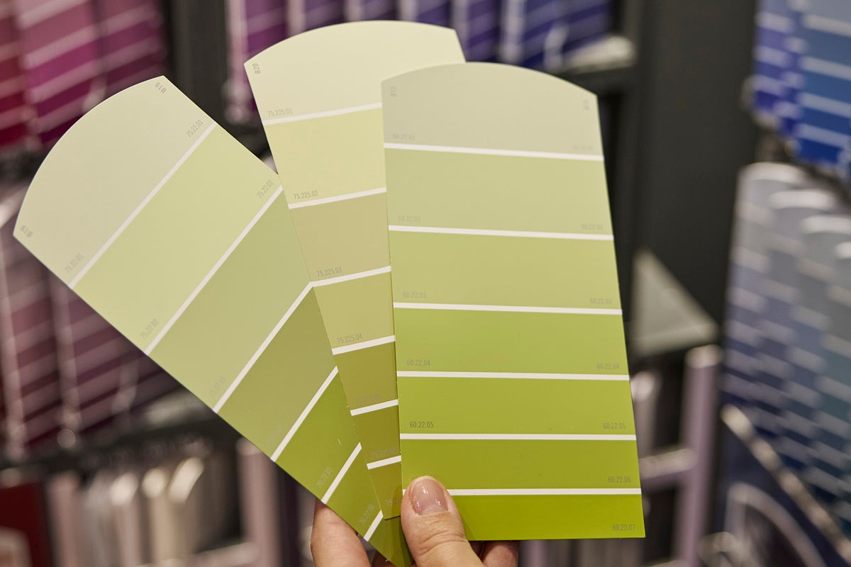 Tre färgkartor med olika nyanser av väggfärg i en hand.
