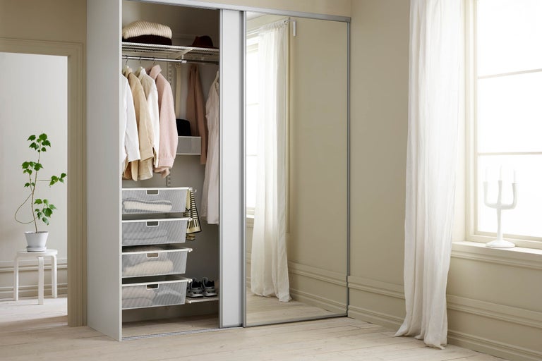 Öppen garderob med skjutdörrar, hyllor, klädstång och trådkorgar för förvaring av kläder och tillbehör.