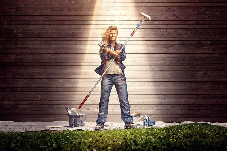 Kvinna med färgroller och pensel framför trävägg