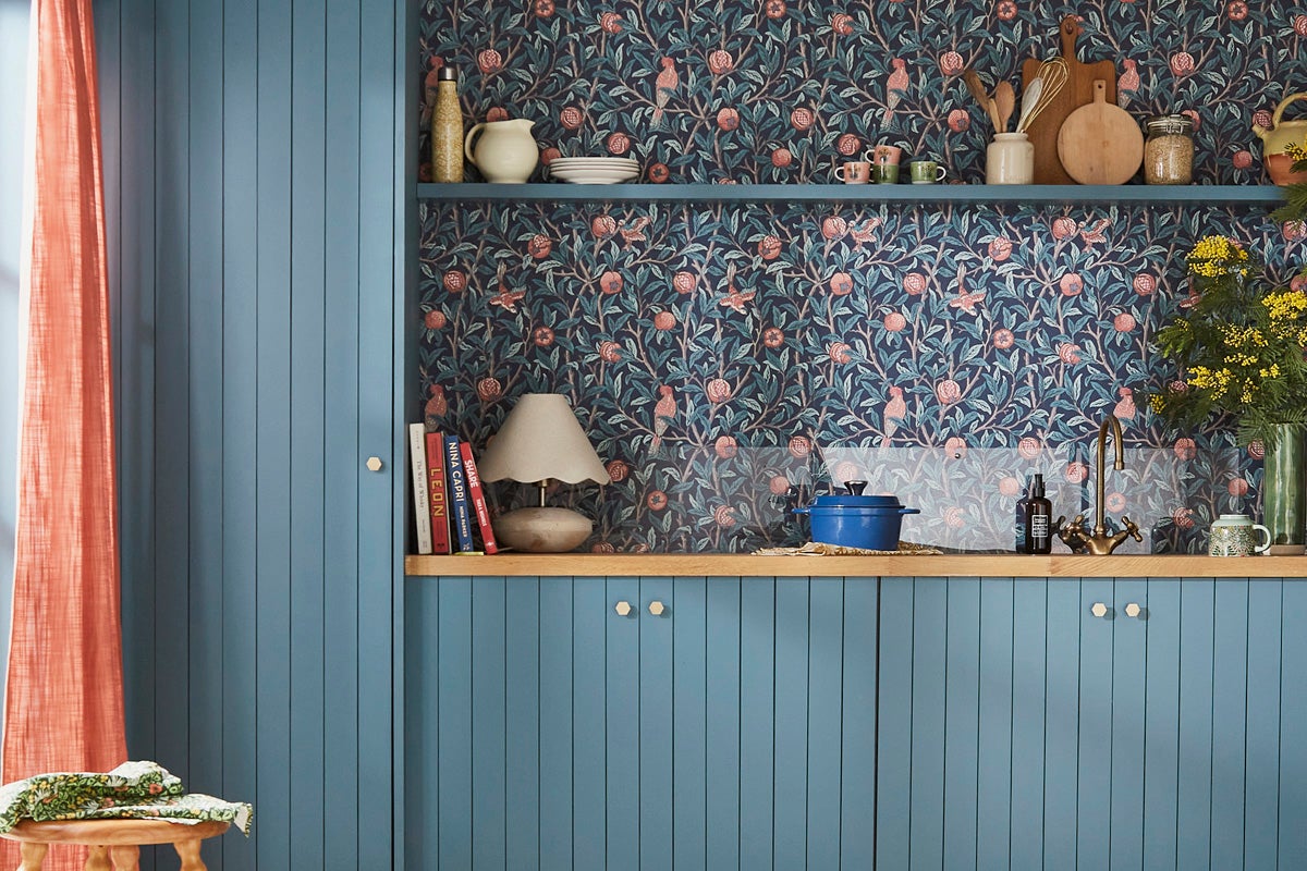 Köksscen med blå skåp, träbänkskiva och mönstrad tapet