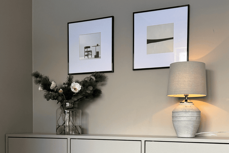 Dekorativt vardagsrum med bordslampa, blomsterarrangemang och inramade bilder.