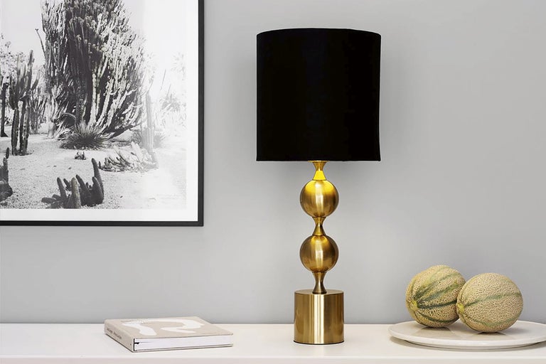 Dekorativ bordslampa med svart lampskärm och gyllene bas på ett bord med dekorationer.