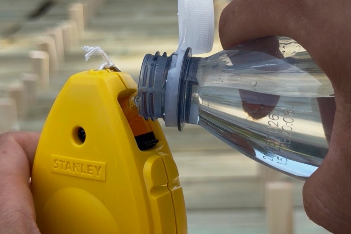En person häller vätska från en plastflaska i öppningen på ett snörslå. Stanley Logo.