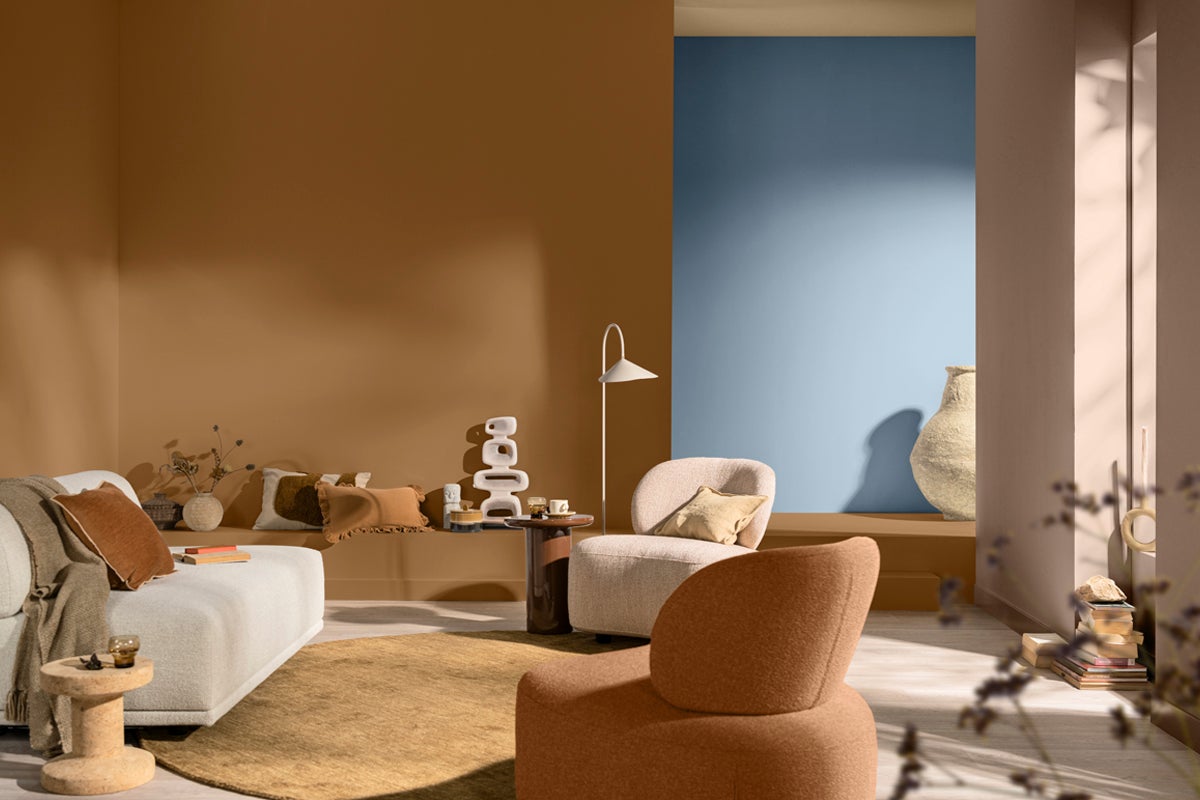 Vardagsrum med soffa, fåtölj och dekorativa element i varma toner.