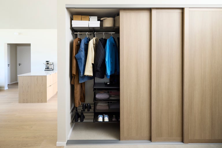 Öppen garderob med skjutdörrar, kläder och förvaringslådor